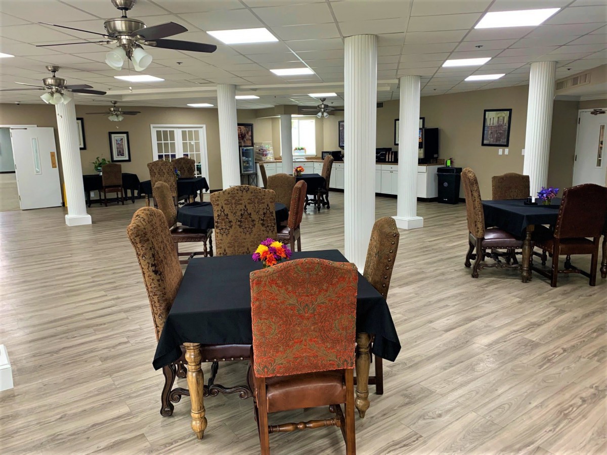 A spacious dining area with multiple tables and chairs, ceiling fans, and a hardwood floor.