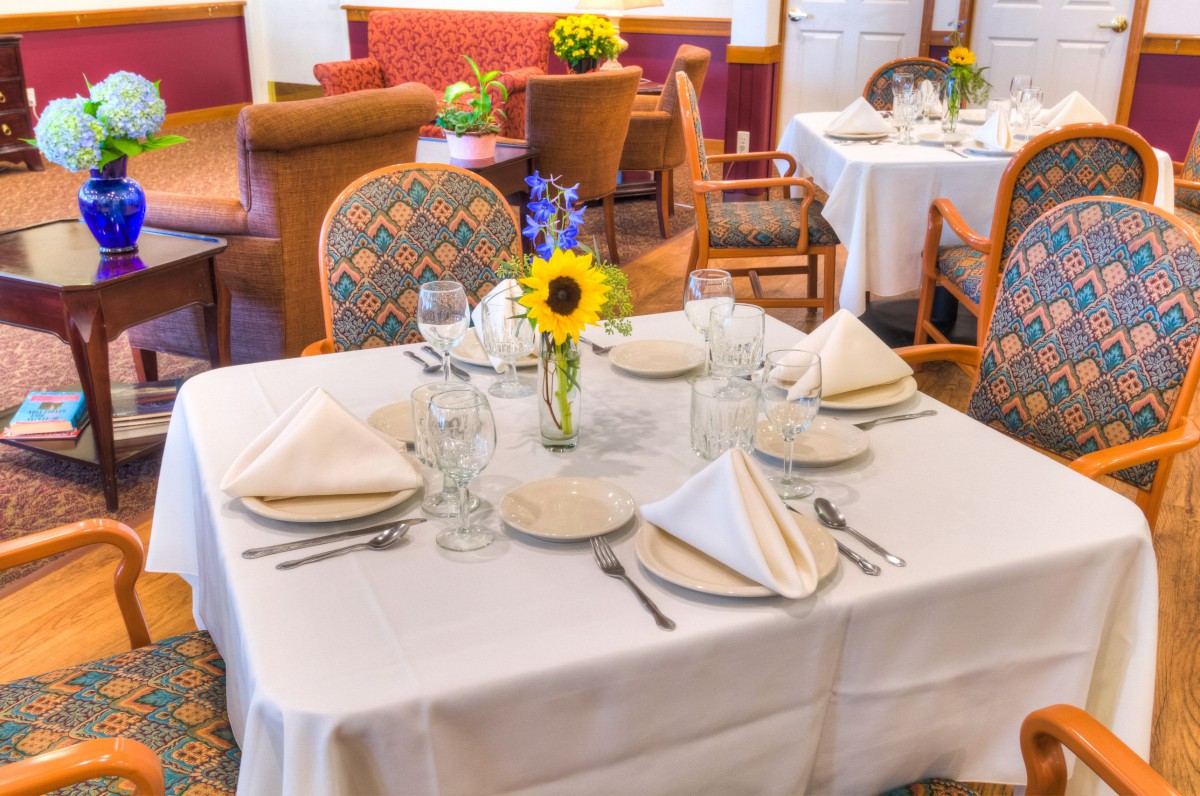 A neatly set dining table with white napkins, glassware, and a floral centerpiece in a restaurant setting.