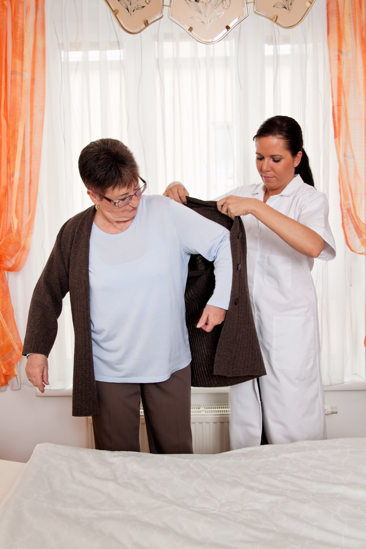 A caregiver assists an elderly person with putting on a jacket.