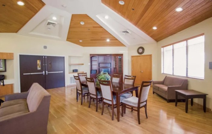 A modern dining area with wooden furniture, featuring a large table surrounded by chairs, a cozy sofa, and warm overhead lighting.