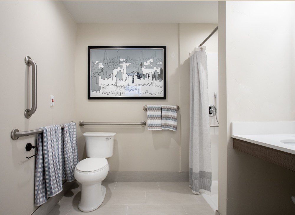 A modern bathroom with a toilet, shower, and neatly arranged towels, featuring a framed artwork on the wall.