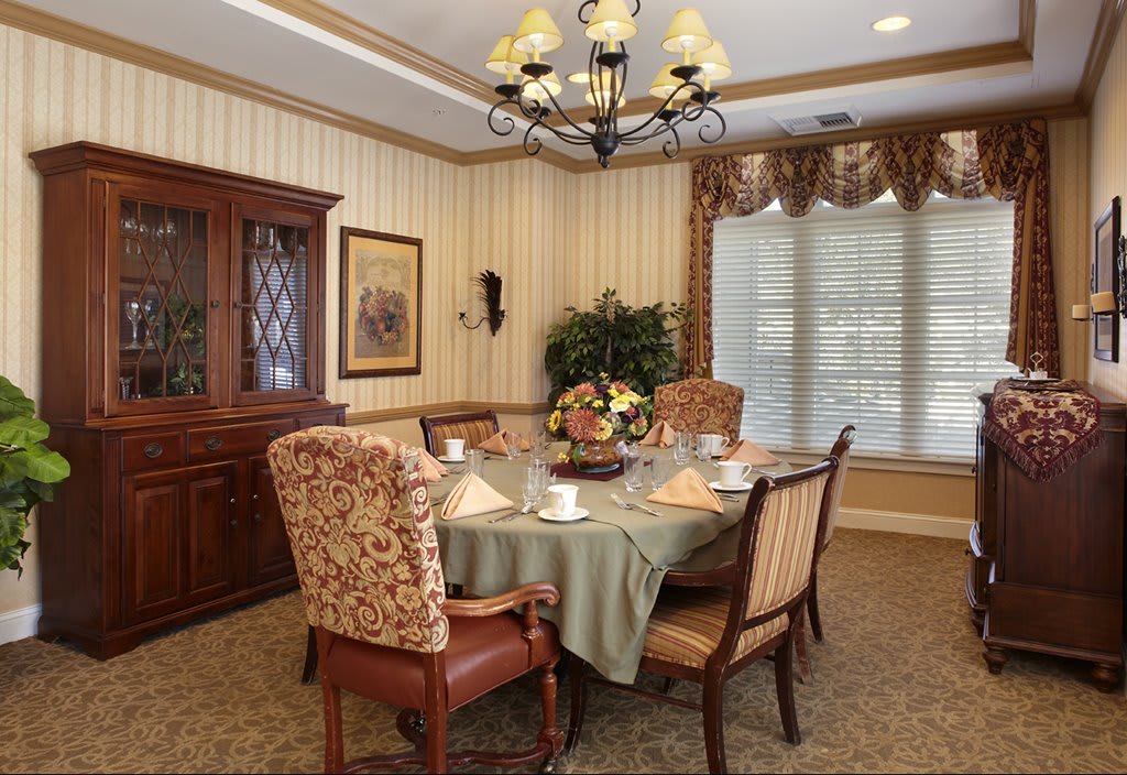 An elegantly decorated dining room featuring a chandelier, a set table with chairs, and a cabinet against striped wallpaper.