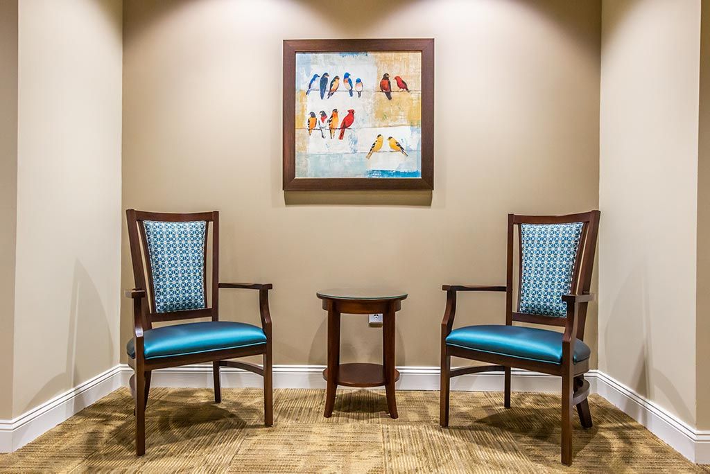A cozy waiting area with two chairs, a small table, and a colorful painting on the wall.