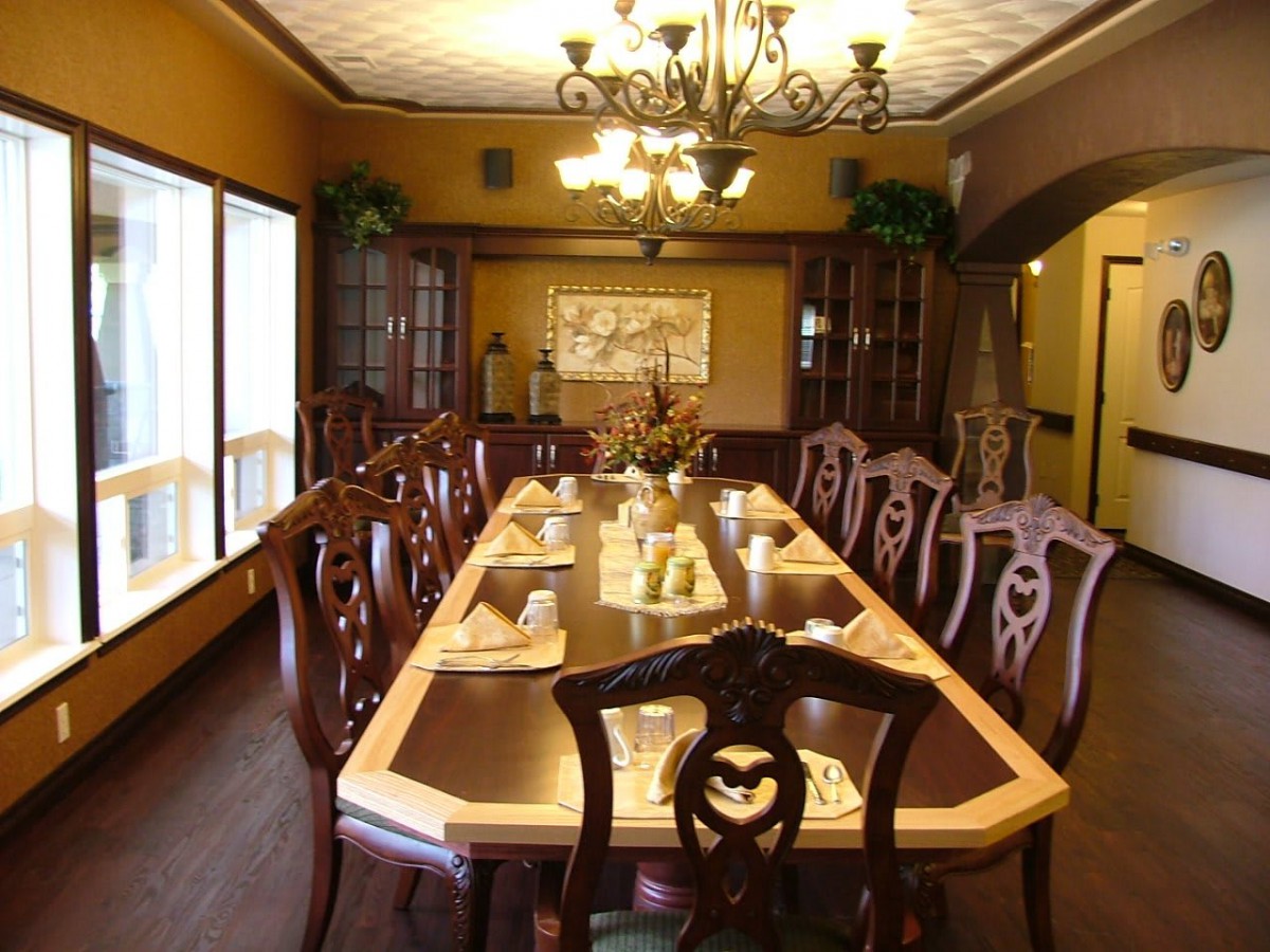 A spacious dining room with an elegant wooden table and chairs, illuminated by a chandelier, featuring a sophisticated table setting.