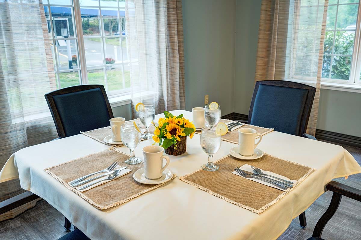 A beautifully set dining table with flowers and tableware near a window.