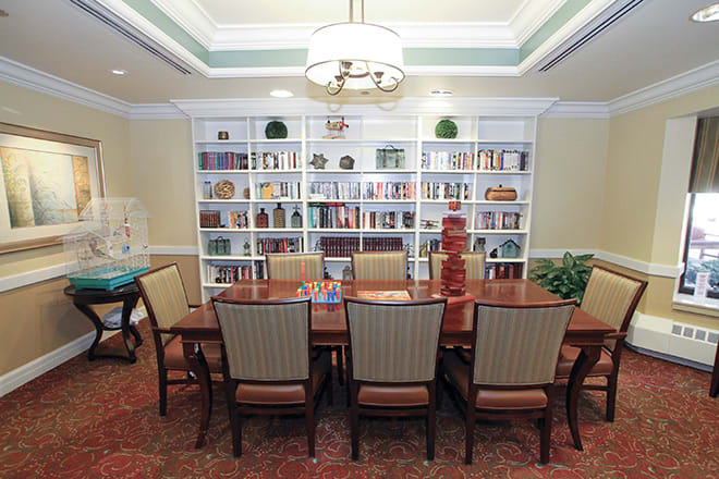 A well-lit library with a large table and chairs, surrounded by bookshelves filled with books.