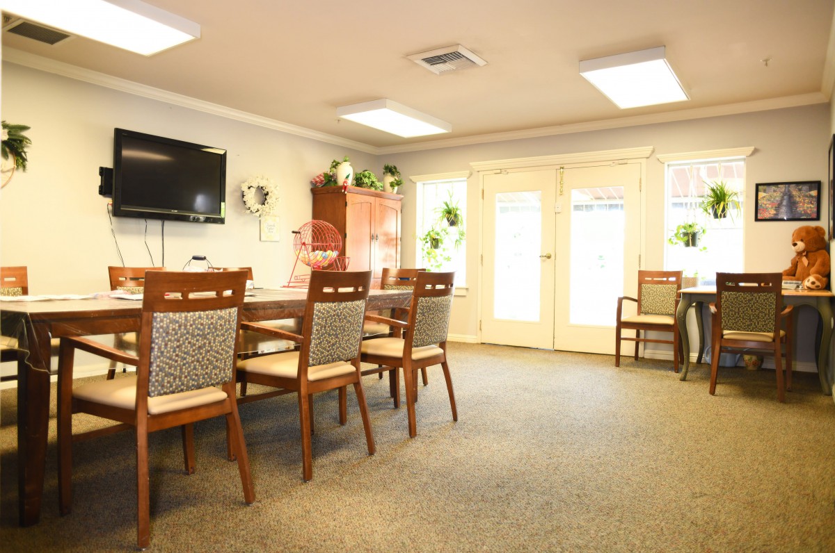 A well-lit dining room with wooden chairs and tables, featuring a television and indoor plants for decor.