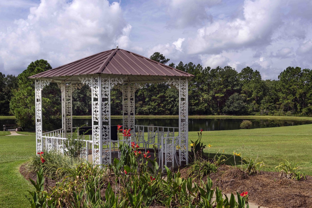 A charming gazebo surrounded by lush greenery under a partly cloudy sky.