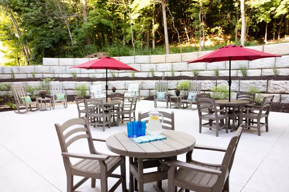 An inviting outdoor patio area with tables, chairs, and umbrellas set against a lush green backdrop.