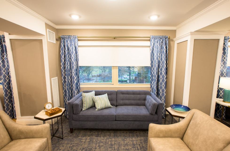 A cozy living room with a blue sofa, patterned curtains, and comfortable chairs.