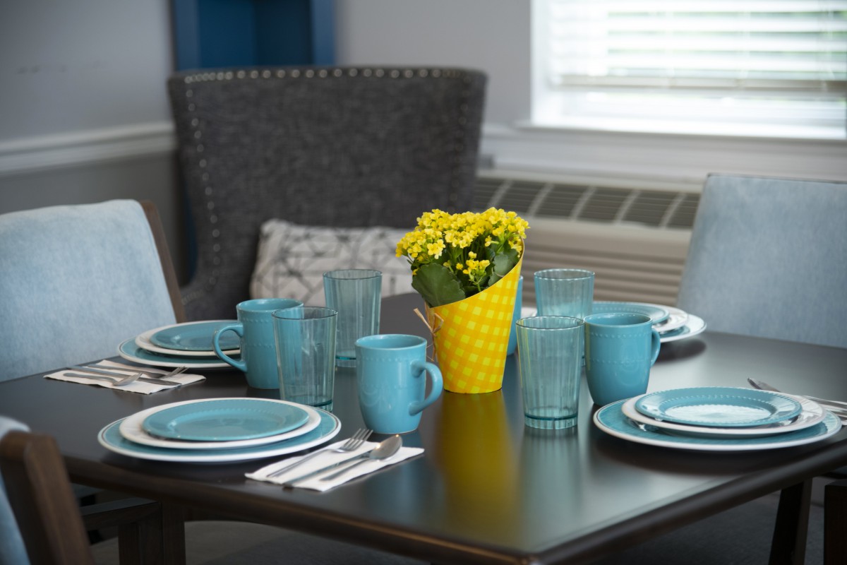 A dining table set with blue dishes and cups, featuring a yellow vase with flowers as the centerpiece.