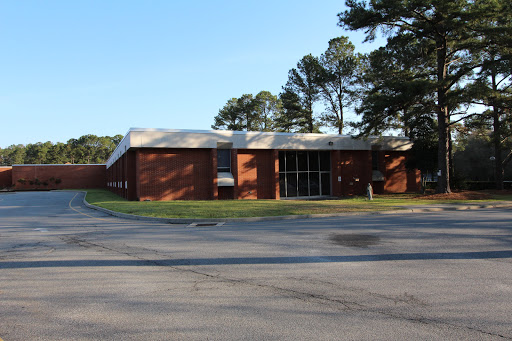 A view of a brick building surrounded by trees, located near a road.