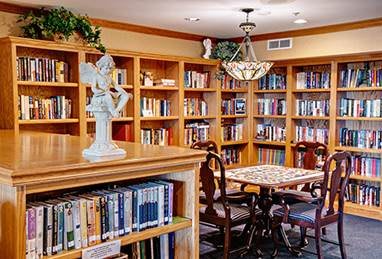 A cozy library with wooden bookshelves, a reading table, and chairs under a decorative chandelier.