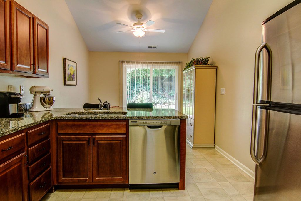 A modern kitchen interior with a dishwasher, wooden cabinets, and a ceiling fan.