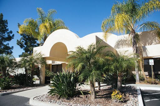A beautiful, modern building surrounded by lush palm trees and vibrant landscaping under a clear blue sky.