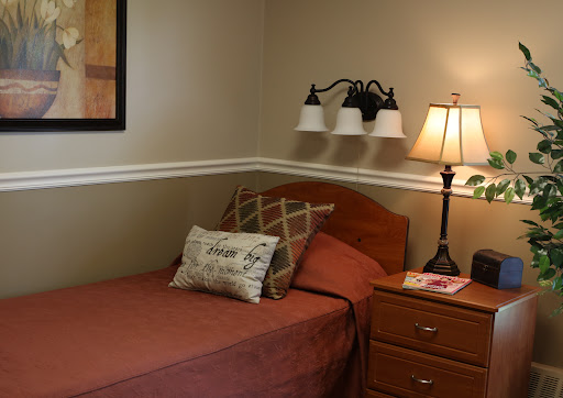 A cozy bedroom featuring a single bed with warm-colored bedding and decorative pillows, accompanied by a bedside lamp and nightstand.