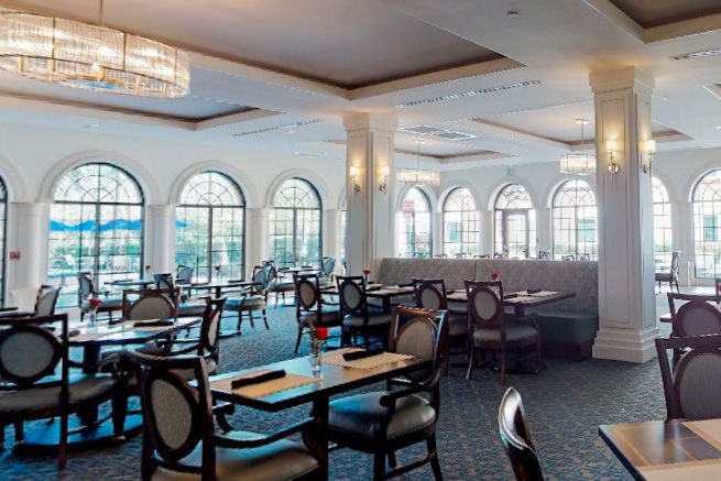 Elegant restaurant dining area with numerous tables and chairs, large windows, and chandeliers.