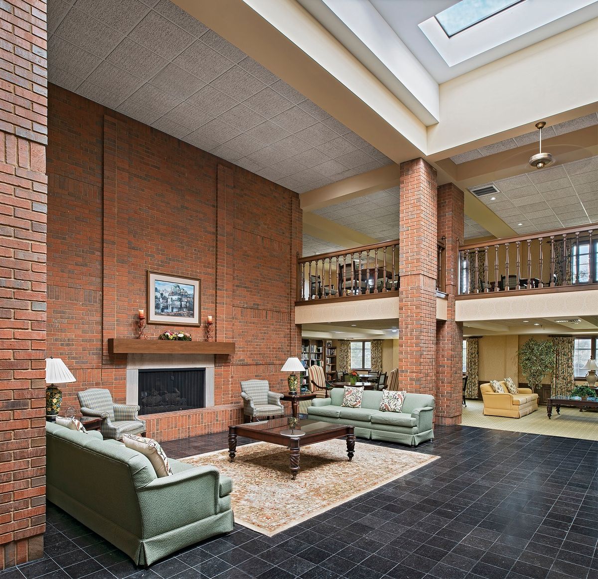 Spacious living room with a brick wall, featuring a fireplace and comfortable seating under a vaulted ceiling with skylights.