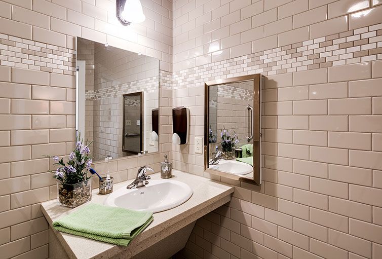 A neatly organized bathroom with tiled walls, featuring a mirror, sink, light fixture, and decorative elements.