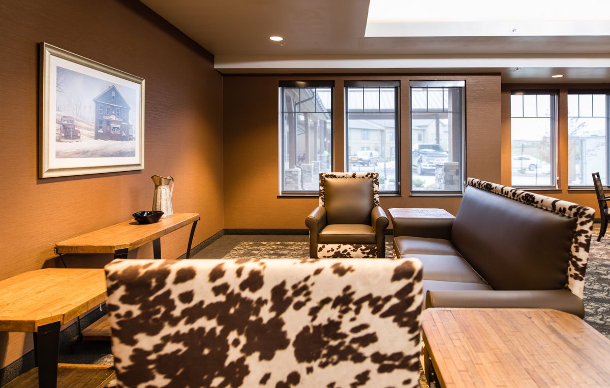 A cozy living room featuring a cowhide-patterned chair, comfortable sofa, and large windows.