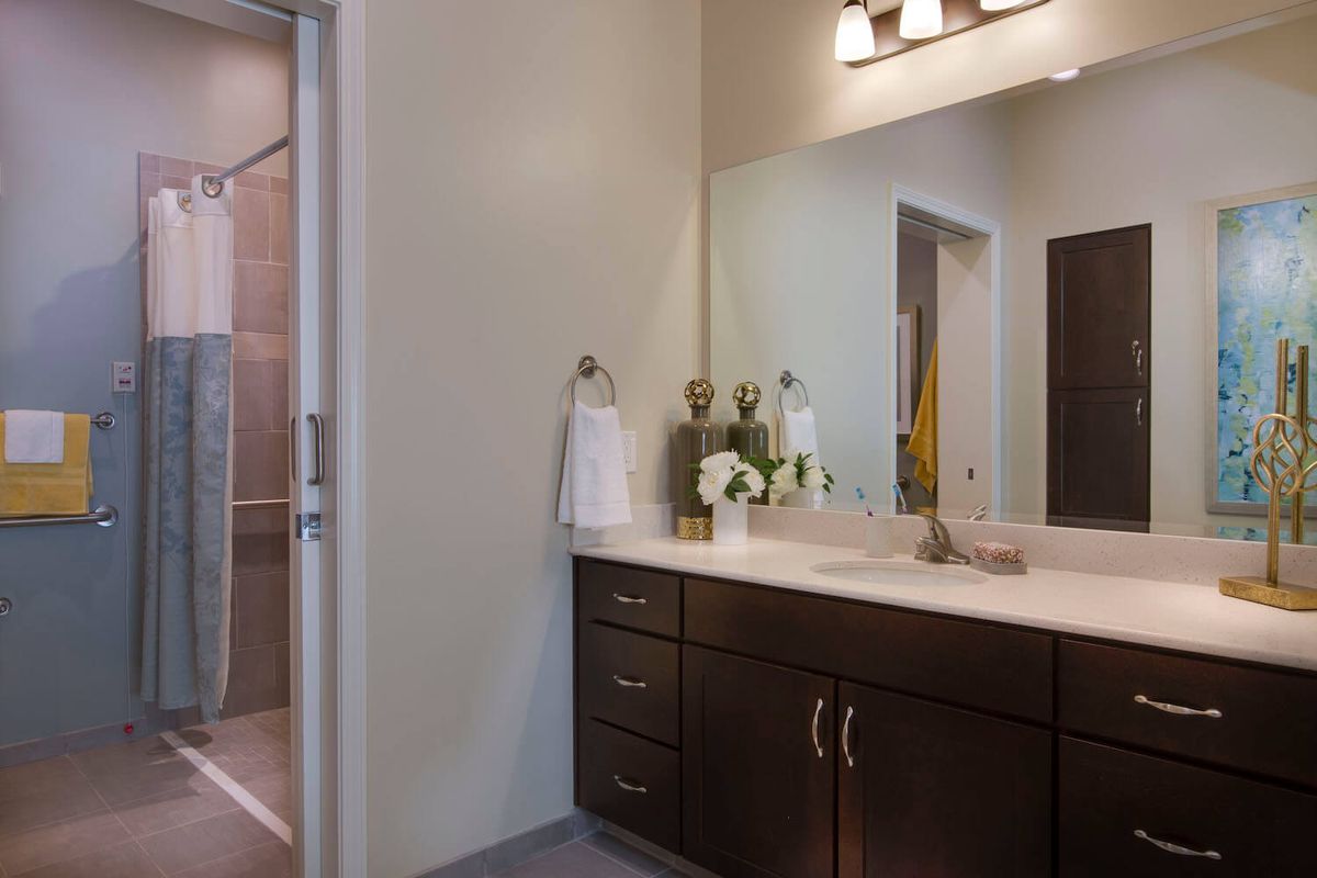 A modern bathroom featuring a spacious sink countertop with dark cabinets and decorative elements like flowers and towels under soft lighting.