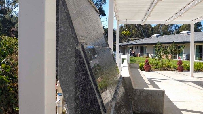 A memorial stone slab with engraved inscriptions, set in an outdoor garden on a sunny day.
