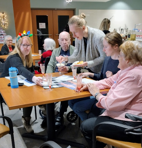 A group of elderly individuals enjoying a social activity at a community center, with a caregiver assisting them.