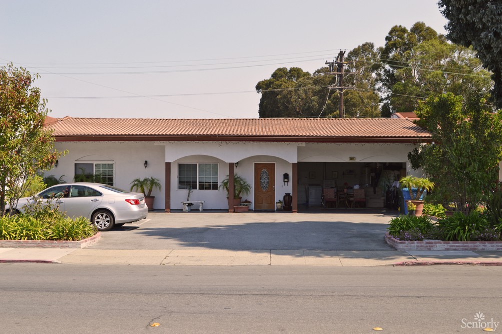 A single-story residential house with a garage and driveway, featuring parked cars and surrounded by trees.