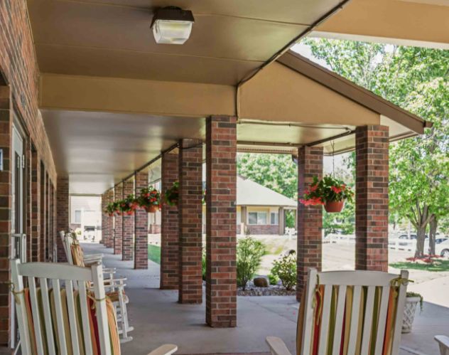 A covered porch area with rocking chairs and hanging plants along brick columns.