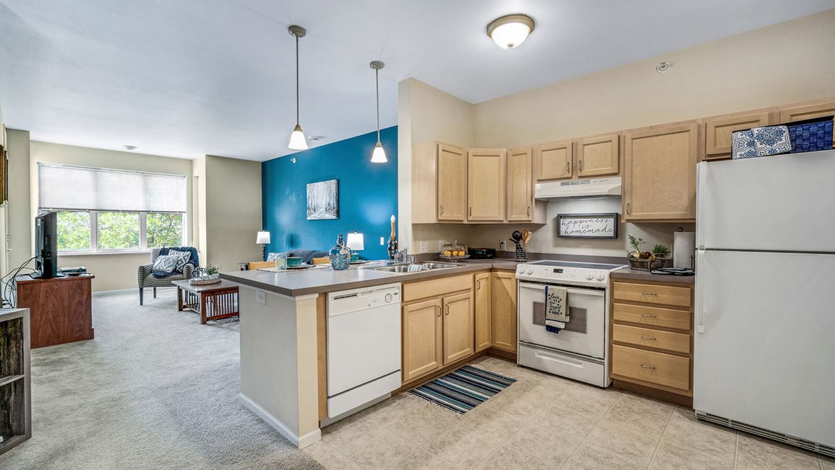 A modern kitchen with an island countertop and wooden cabinets, adjacent to an open living area.