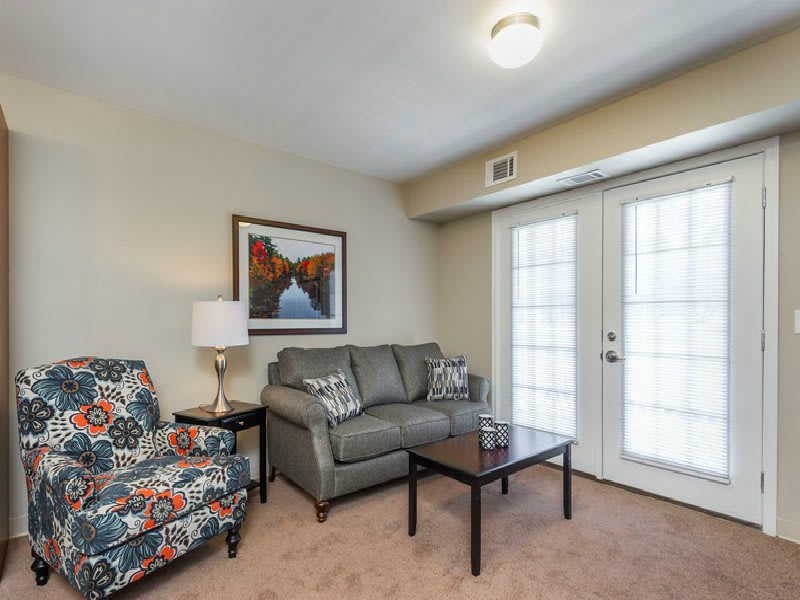 A cozy living room with a gray sofa, colorful armchair, and coffee table near French doors.