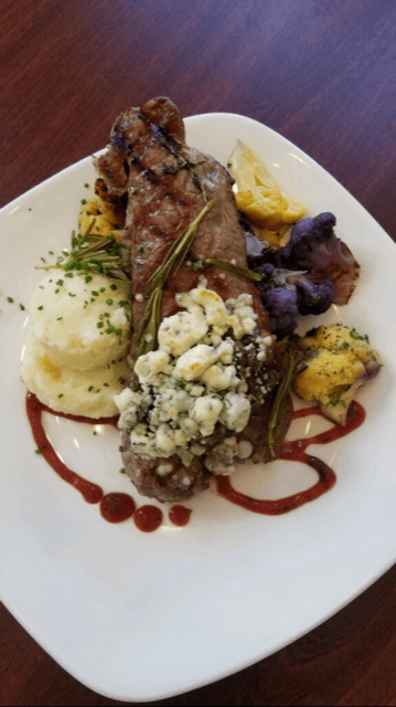 A gourmet steak dish garnished with blue cheese, rosemary, and served alongside mashed potatoes.