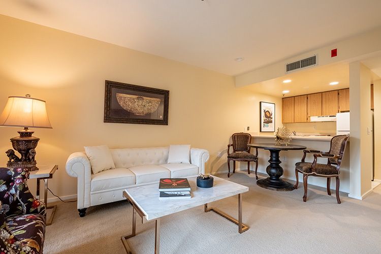 A cozy living room with a white sofa and a marble coffee table, featuring artwork on the wall and an adjacent dining area.