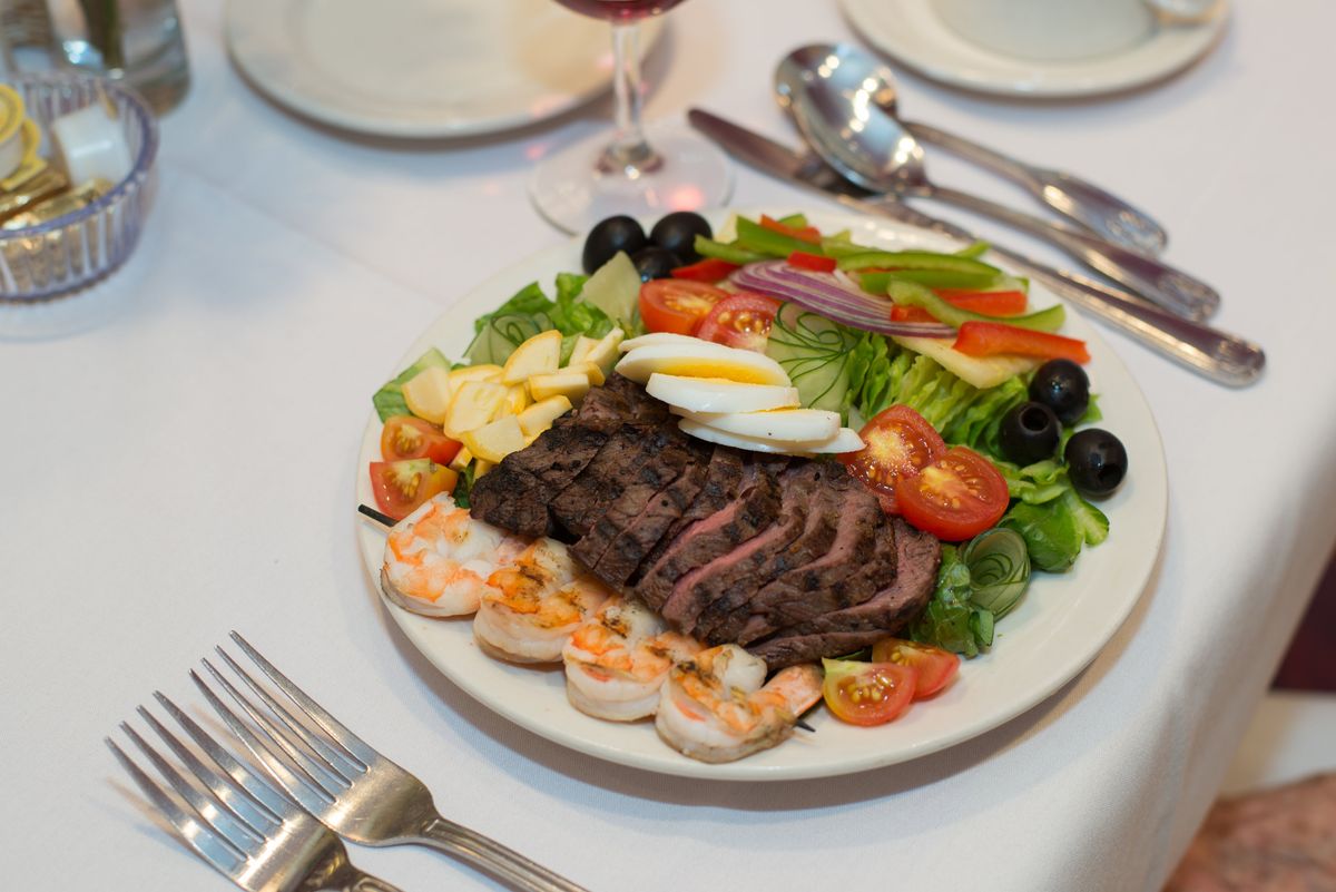 A gourmet dinner plate featuring steak, shrimp, and a fresh salad with various vegetables.