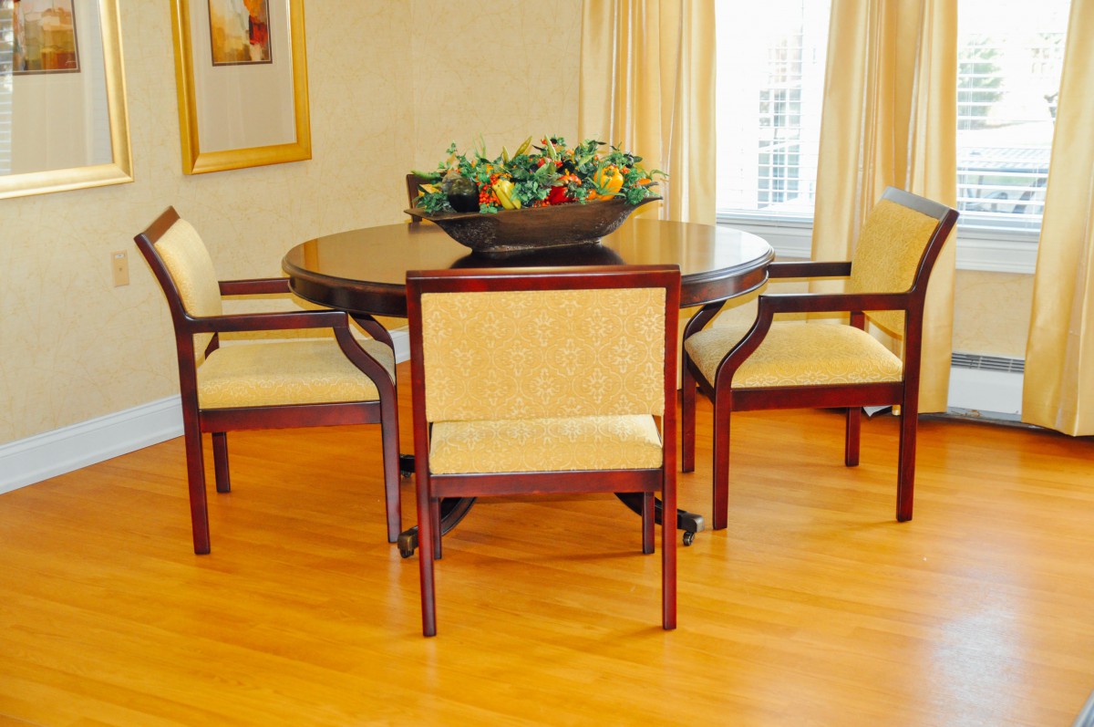 A cozy dining area featuring a round wooden table with four chairs and a decorative fruit bowl centerpiece.