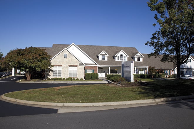 A suburban residential building with a front yard and clear blue sky.
