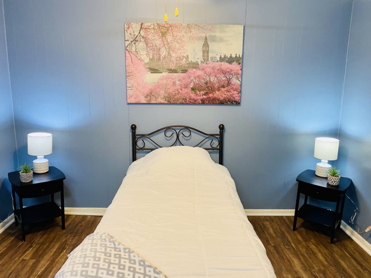 A cozy bedroom with a single bed, flanked by nightstands and lamps, featuring wall art above the headboard.