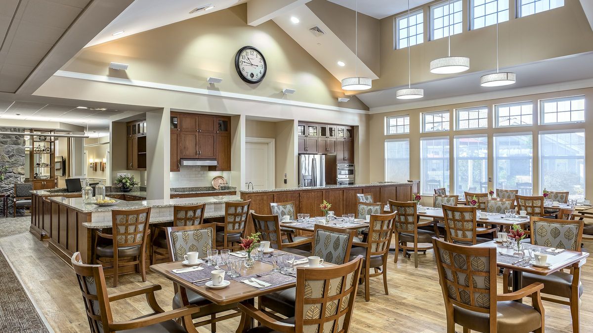 A well-lit dining area with multiple tables and chairs, featuring a large clock on the wall.