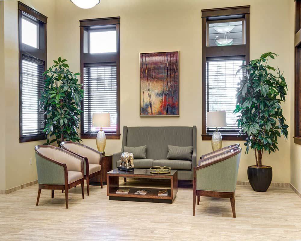 A cozy living room with a sofa, chairs, and a coffee table surrounded by greenery and natural light.
