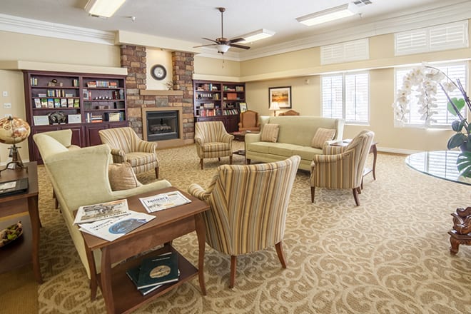 A cozy living room with sofas and armchairs arranged around a fireplace, surrounded by bookshelves and a side table.
