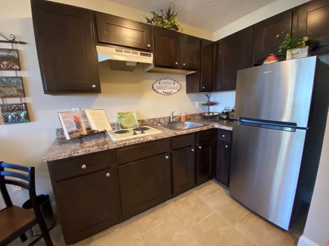 A cozy kitchen with dark wooden cabinets, a stainless steel refrigerator, and a compact stove.