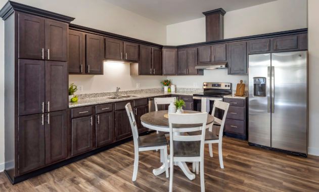 A modern kitchen with dark wooden cabinets, a round dining table, and stainless steel appliances.