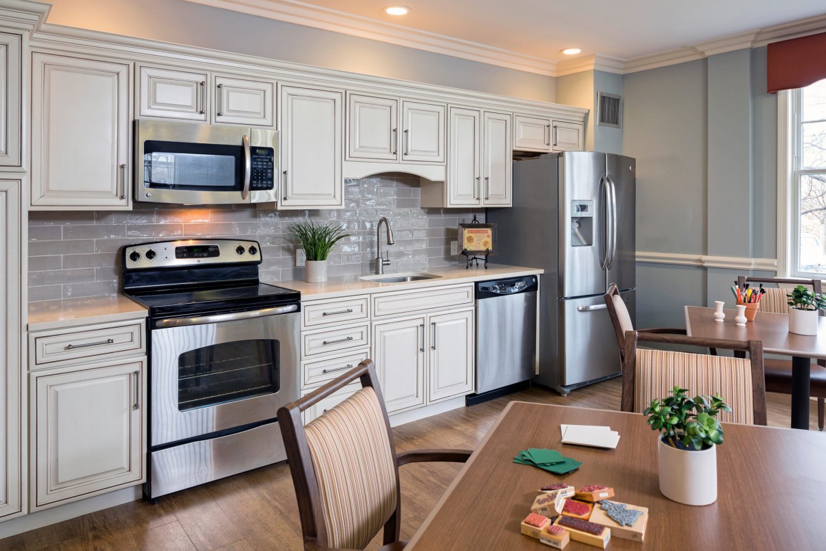 A modern kitchen with white cabinets, stainless steel appliances, and a dining area.