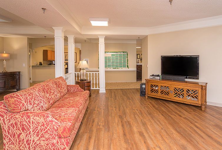 A cozy living room with a wooden floor, featuring a patterned sofa and a television on a stand.