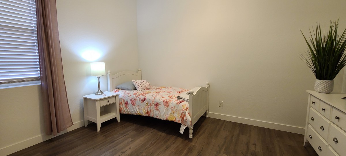 A minimalist bedroom with a single bed, lamp, and nightstand on wooden flooring.