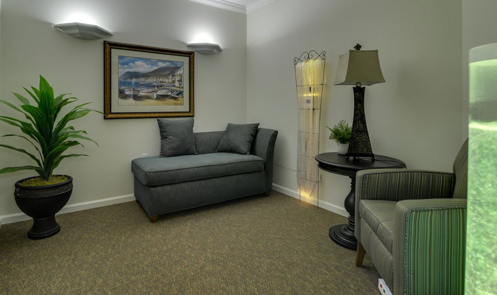 A cozy living room with a dark gray couch, a small round table, and a floor lamp. A painting hangs on the wall above the couch.