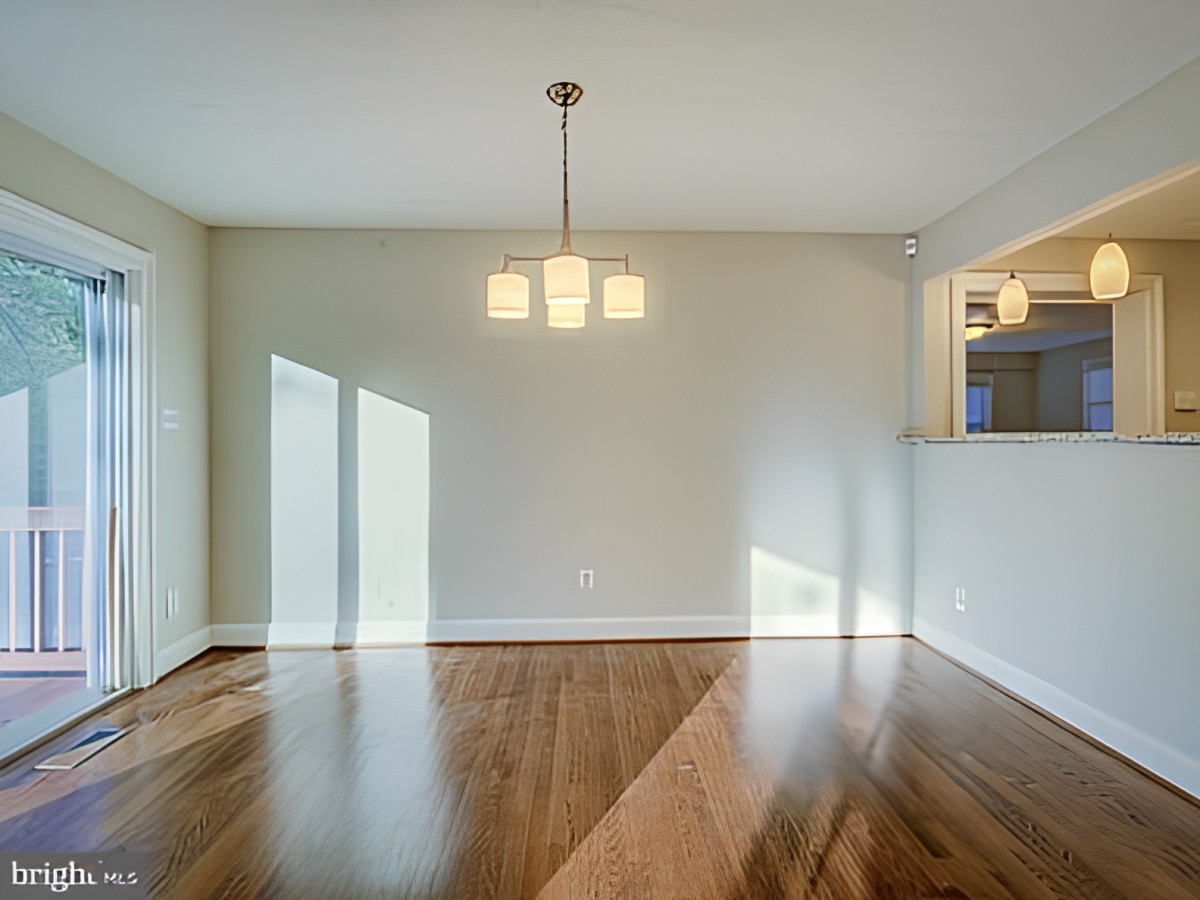 An empty dining room with hardwood floors and a hanging light fixture.