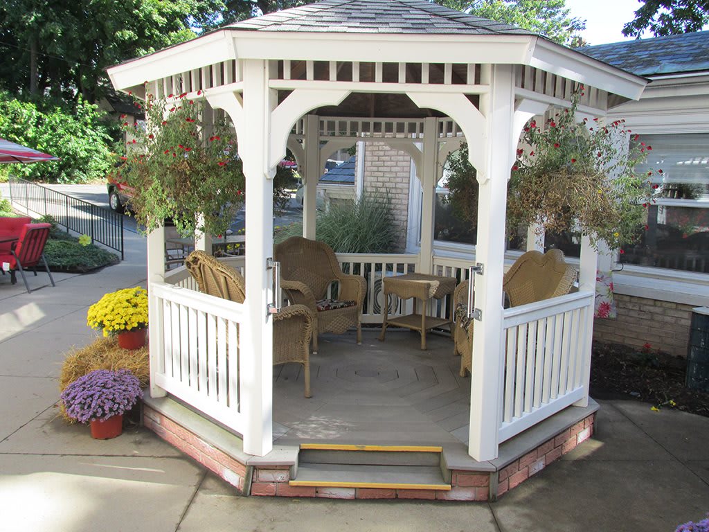 A charming gazebo with wicker chairs and hanging plants offers a cozy outdoor retreat.