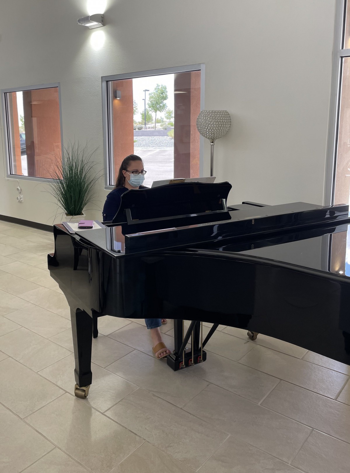 A person wearing a mask plays a grand piano indoors.