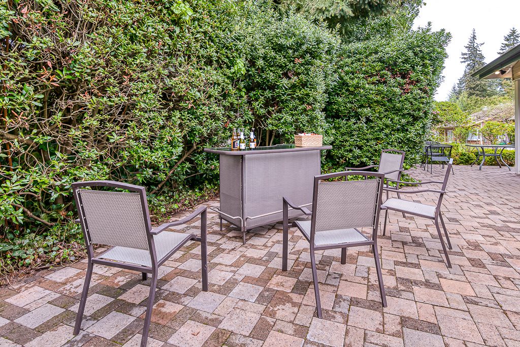 A cozy outdoor patio setup with chairs and a table surrounded by lush greenery.